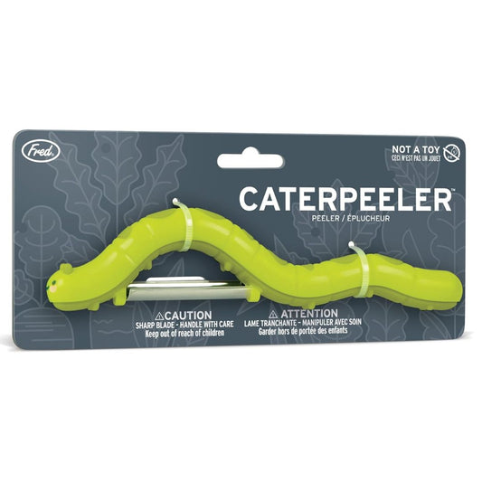 A green caterpillar-shaped peeler tool in retail packaging on a white background. The card shows the brand Fred.