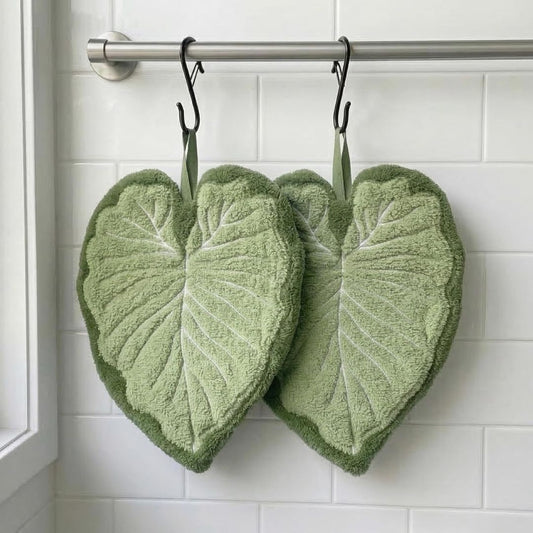 Two green heart-shaped hand towels with leaf-like embossed patterns hang from black hooks on a metal rod against a white tiled wall.