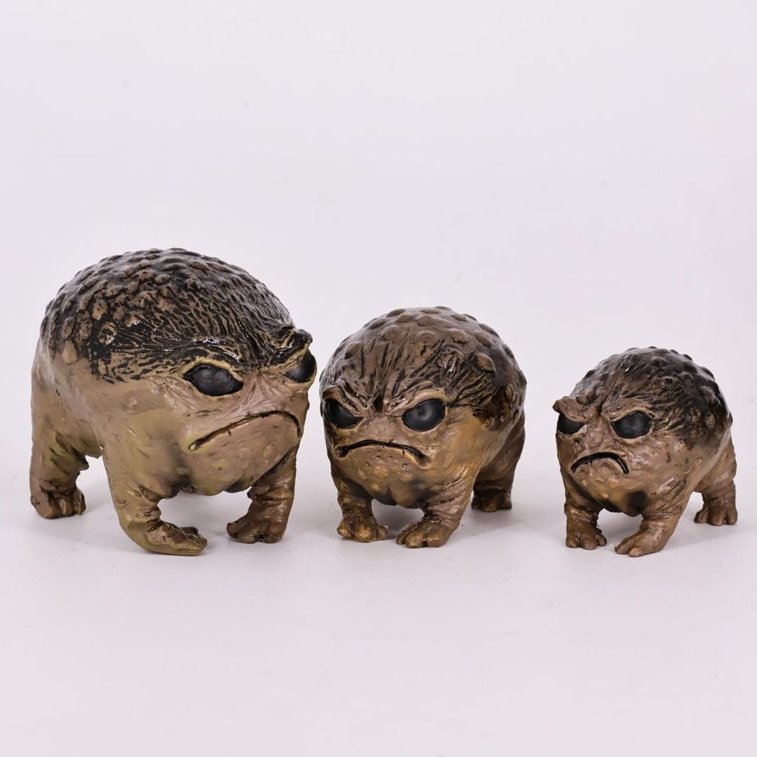 Three small textured angry frog figurines in a row, varying in size, with a distressed metallic bronze and black finish, set against a plain white background.