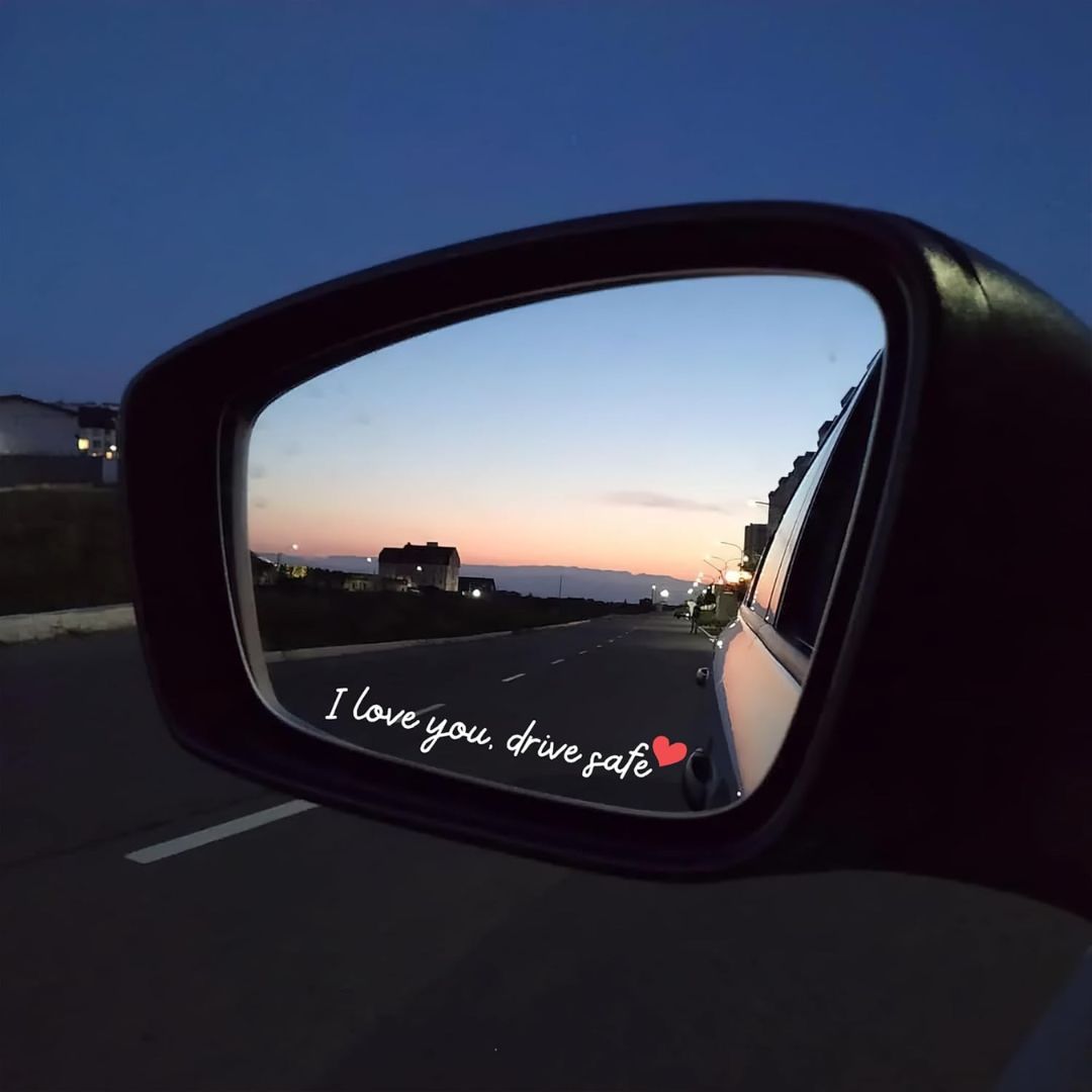 Car side mirror with 'drive safe, I love you' sticker at sunset.