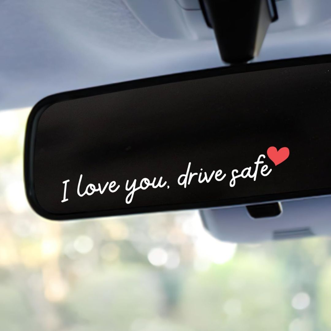 Car rearview mirror with an 'I love you, drive safe' sticker and heart symbol.