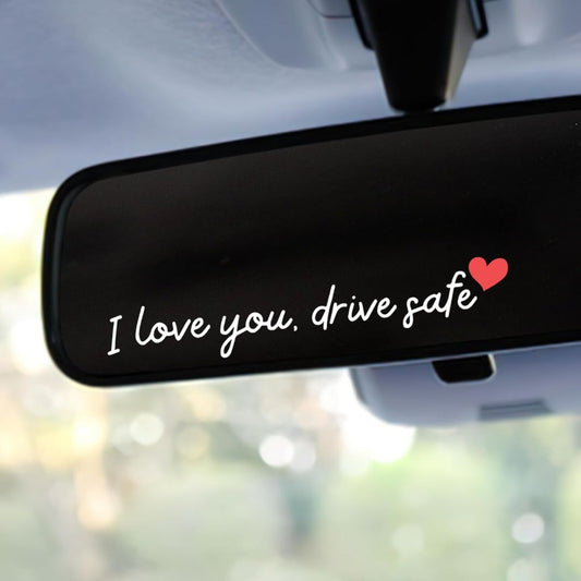 Car rearview mirror with an 'I love you, drive safe' sticker and heart symbol.