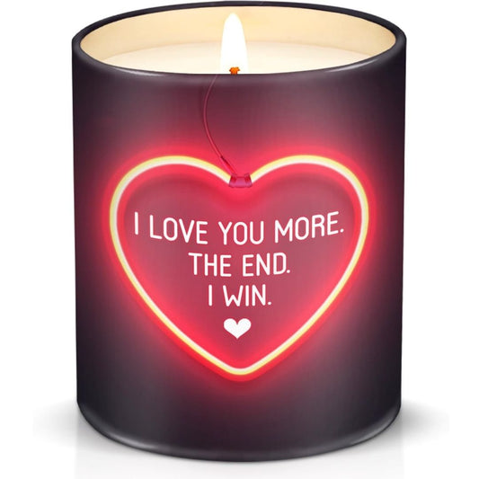 A dark purple cylindrical candle with a lit wick and a glowing red heart-shaped neon design on the front that reads, 'I LOVE YOU MORE. THE END.