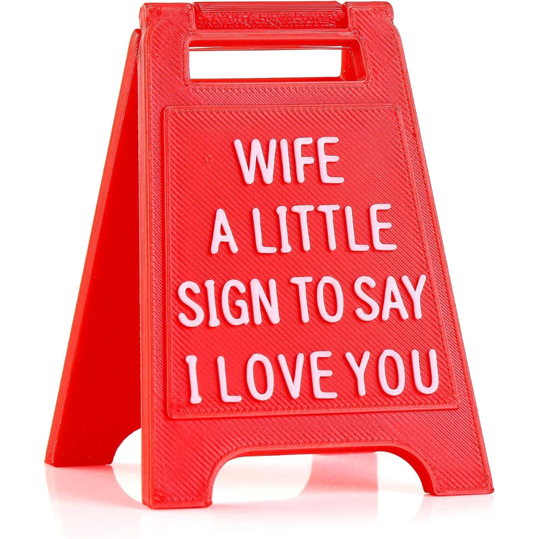 A red plastic A-frame sign with white raised text reading 'WIFE A LITTLE SIGN TO SAY I LOVE YOU' on a clean white background.