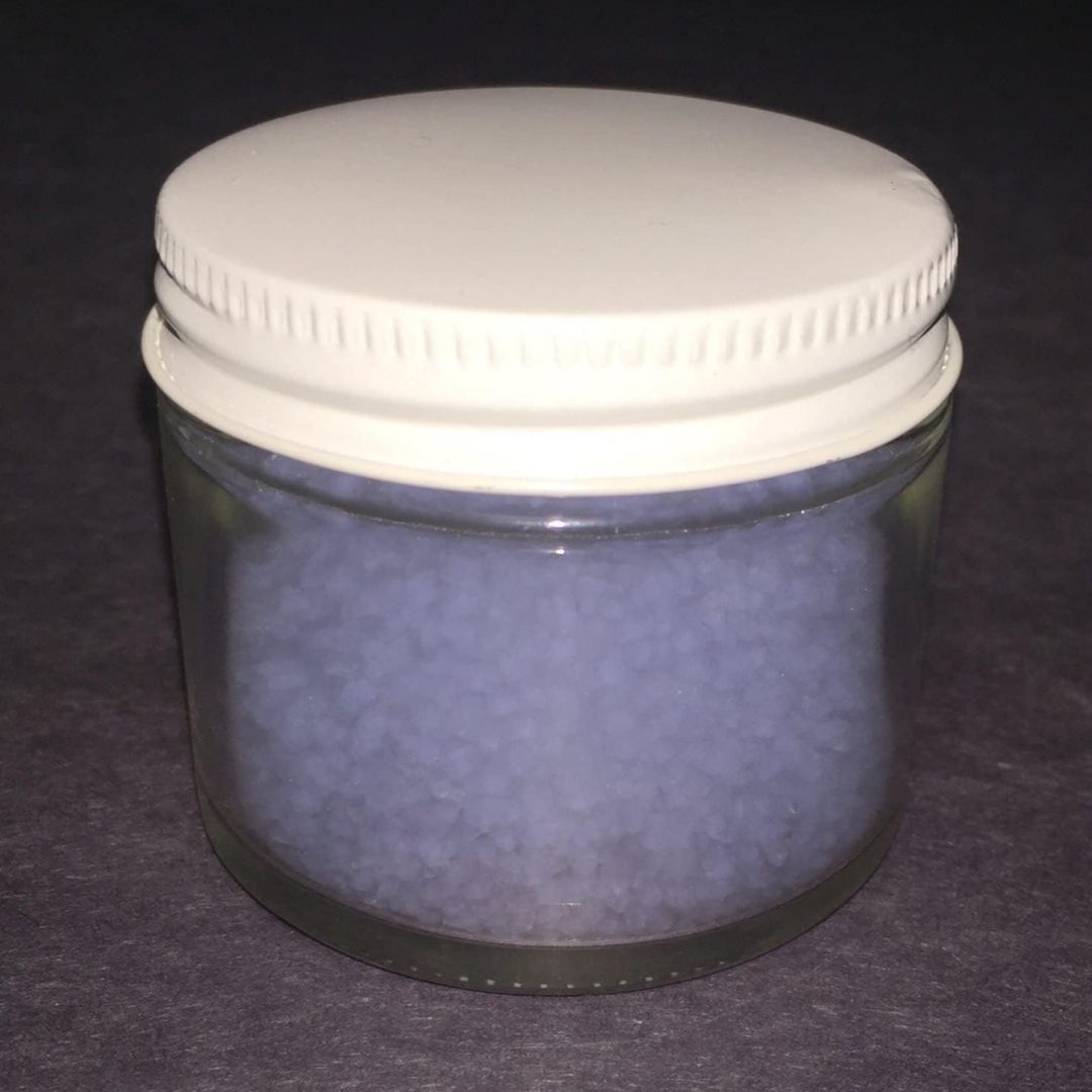 A clear glass jar filled with silica aerogel frozen smoke, sealed with a white screw-top lid, set against a dark gray background.