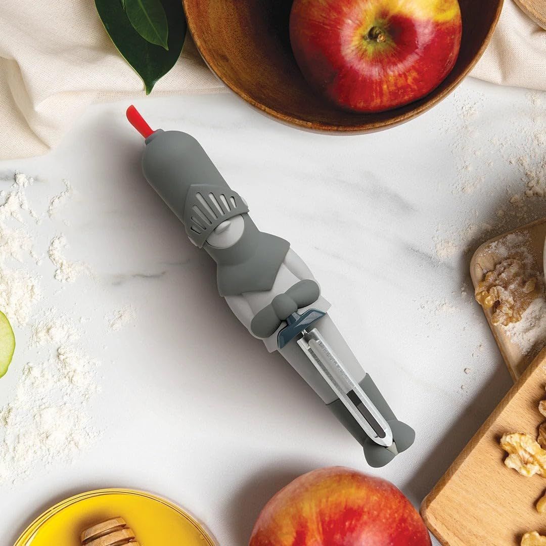 Gray vegetable peeler shaped like a knight on a marble surface with apples and flour in the background