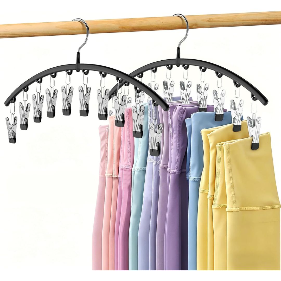 Two black arched garment organziers with multiple silver spring clips, hanging from a wooden rod. Several colorful garments in pink, light blue, lavender, purple, navy, and yellow are clipped to the hangers against a plain white background.