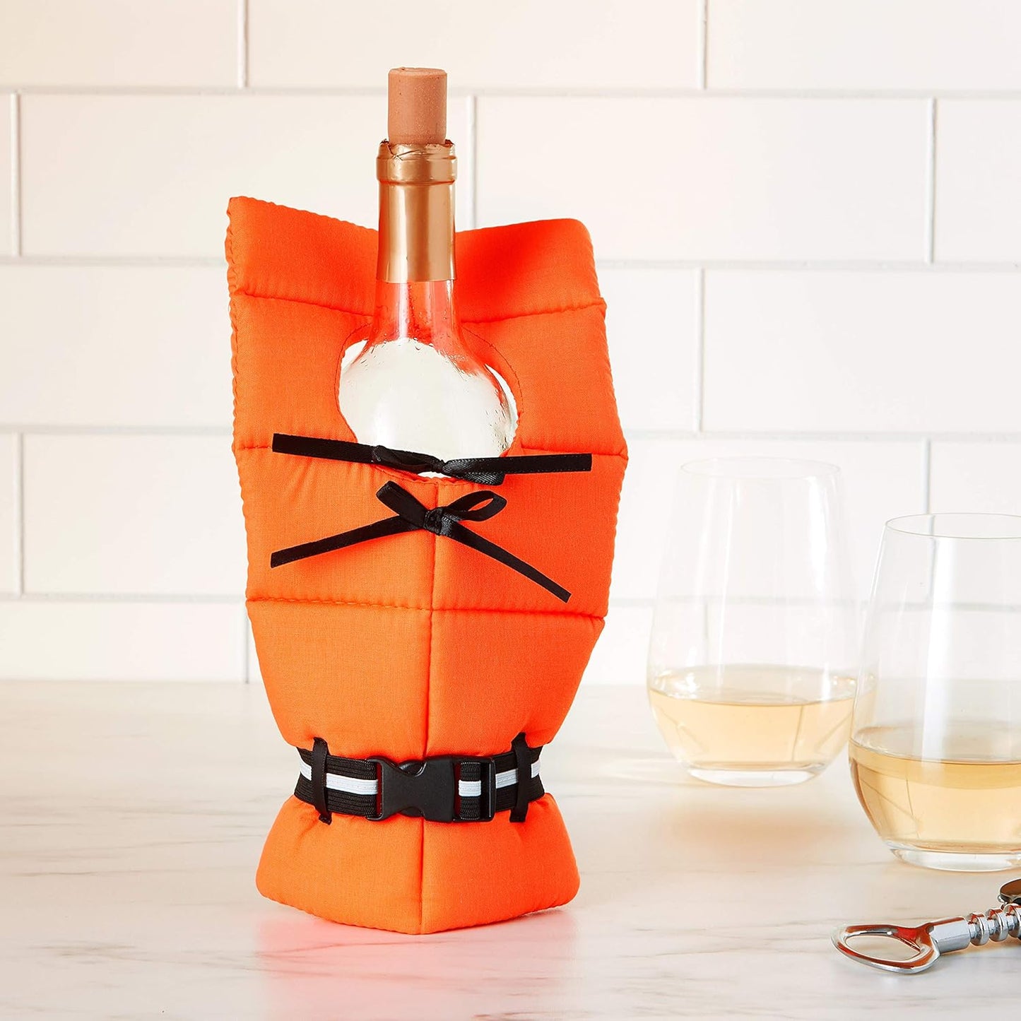 Wine bottle in an orange life jacket cover with a white tiled wall background, two glasses of rosé, and a bottle opener on a marble counter—nautical vibes meet kitchen chic!