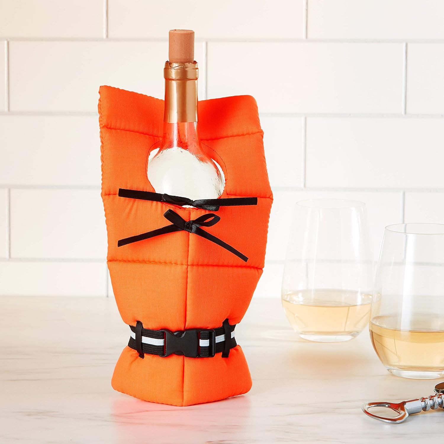 Wine bottle in an orange life jacket cover with a white tiled wall background, two glasses of rosé, and a bottle opener on a marble counter—nautical vibes meet kitchen chic!