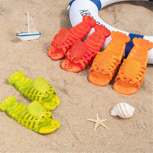 Colorful lobster-shaped sandals on sand with a toy boat and shell nearby