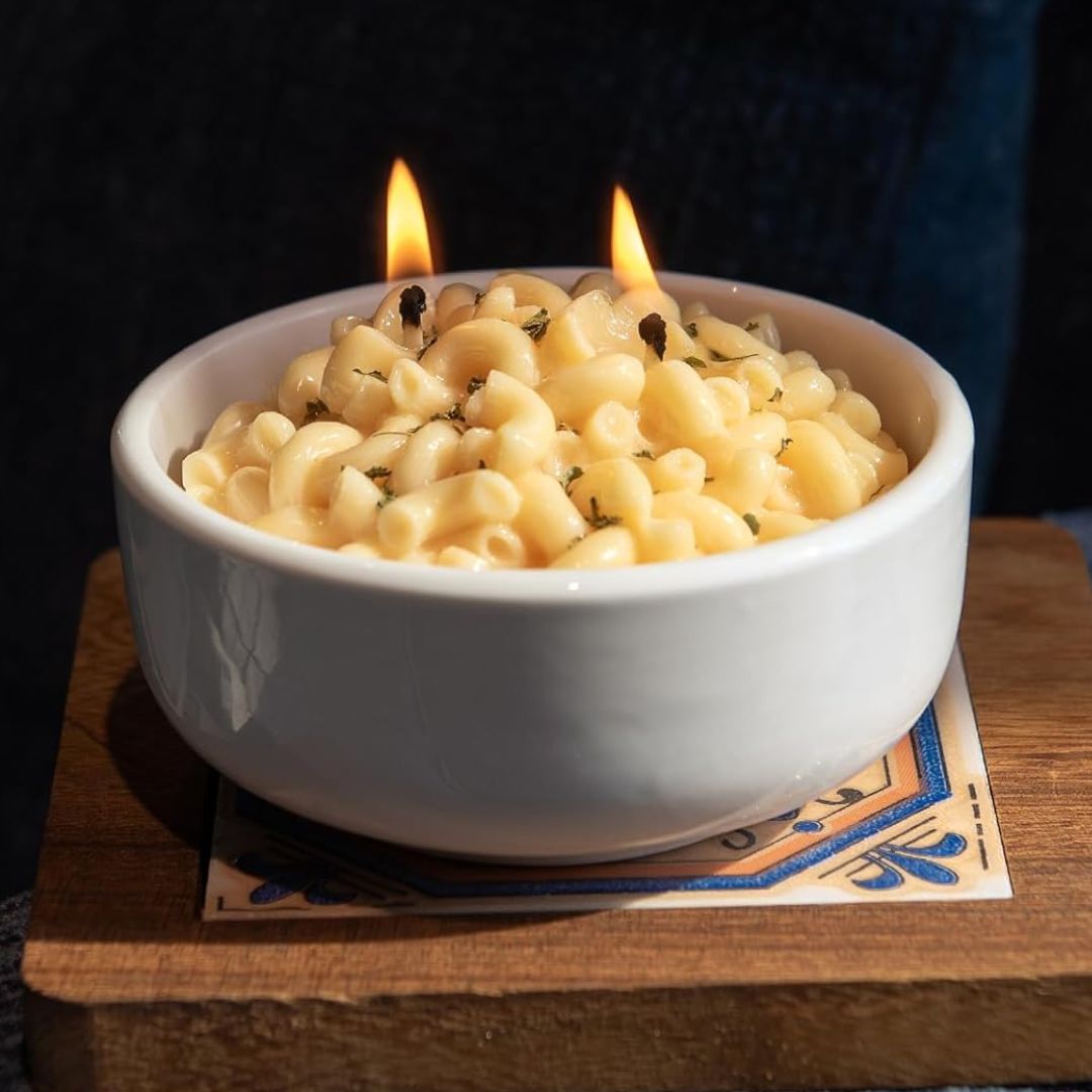 Macaroni and cheese candle with two flames in a bowl on a dark background