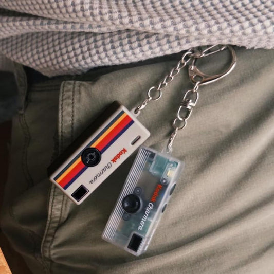 Two mini retro keychain digital cameras attached to a persons belt clip