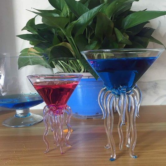 Two octopus-shaped cocktail glasses with red and blue drinks on a wooden surface.