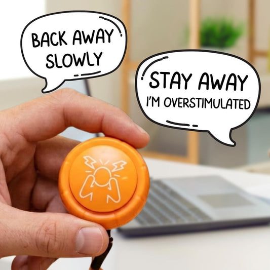 A hand holds an orange emergency stop button with a white lightning-bolt symbol. Speech bubbles read 'BACK AWAY SLOWLY' and 'STAY AWAY I'M OVERSTIMULATED' against a blurred office background with a laptop.