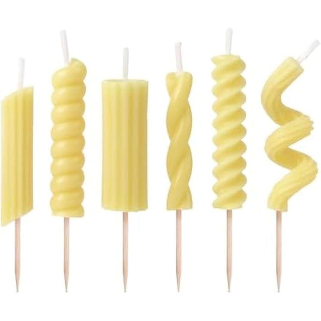 Set of yellow pasta shaped candles with wooden sticks against a white background
