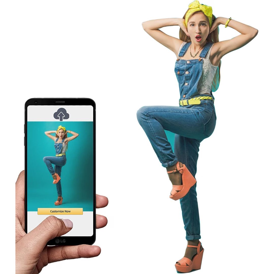 A hand holds a smartphone showing a digital app preview of a person in denim overalls and jeans, while the same person appears larger on the right in a posed standing pose against a plain white background as a life size cutout