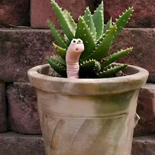 Potted plant with a worm shaped water sensor emerging from it against a brick wall background