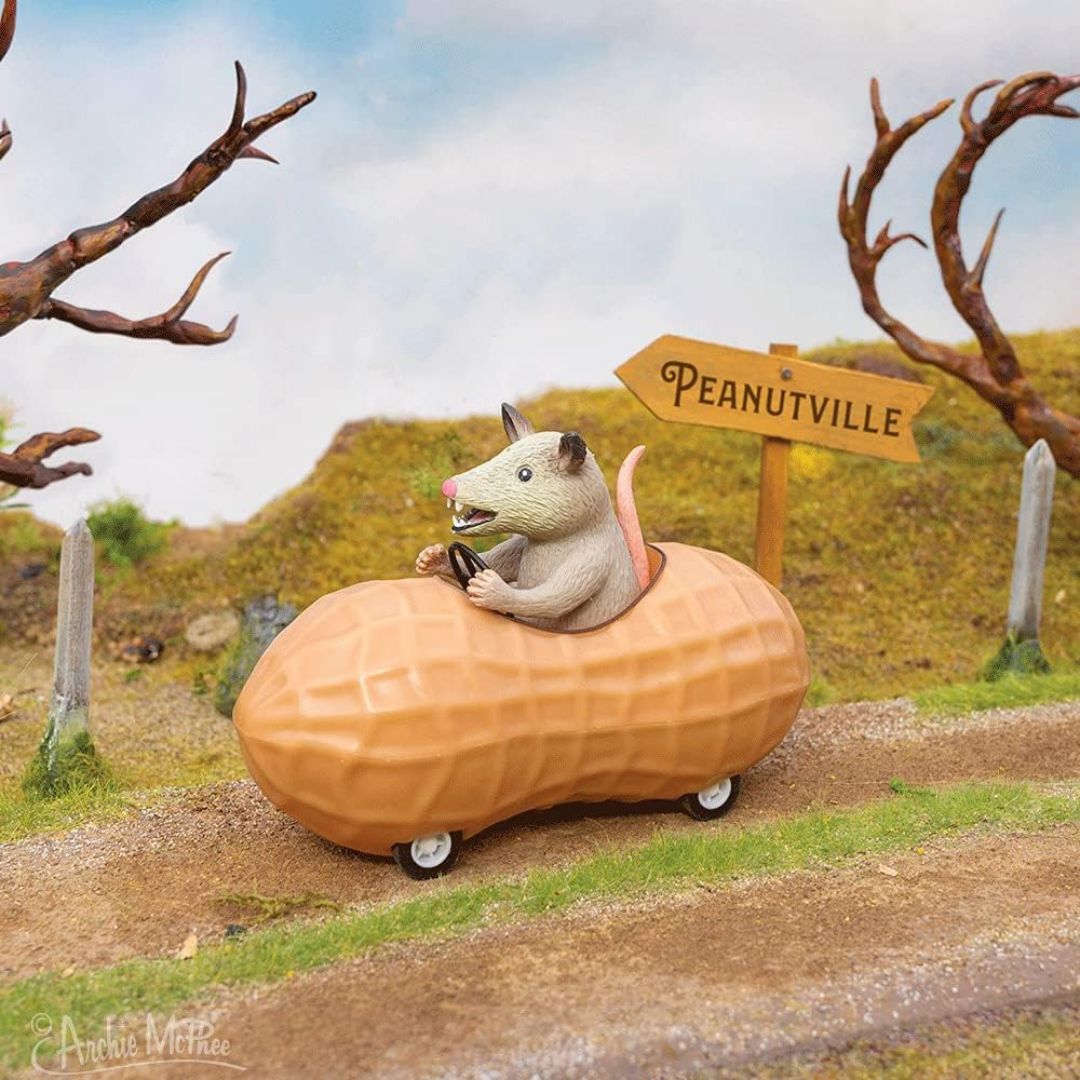 Archie McPhee possum driving a peanut-shaped pull back toy car past a Peanutville sign