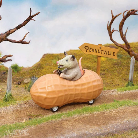 Archie McPhee possum driving a peanut-shaped pull back toy car past a Peanutville sign
