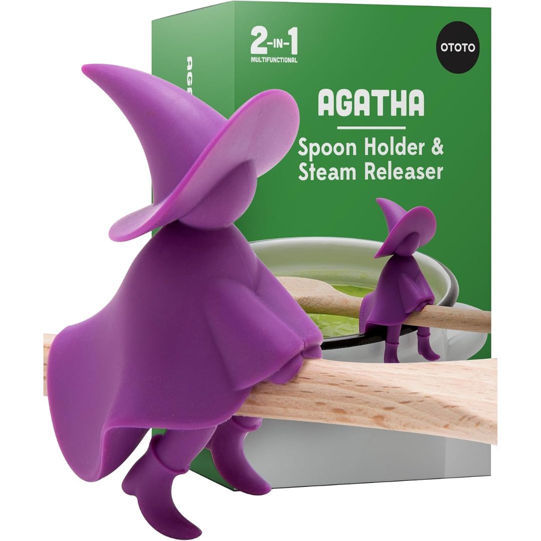 A purple Agatha Spoon Holder and Steam Release clip shaped like the Morte Noire character, shown in front of its green retail box on a white background.