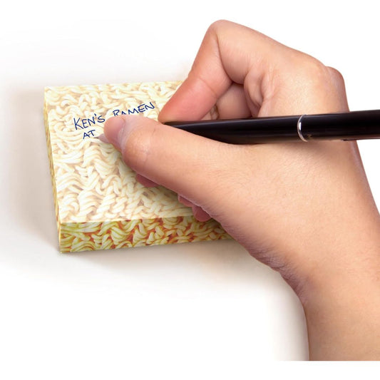Hand writing on a small pad of ramen noodle sticky notes with a pen.