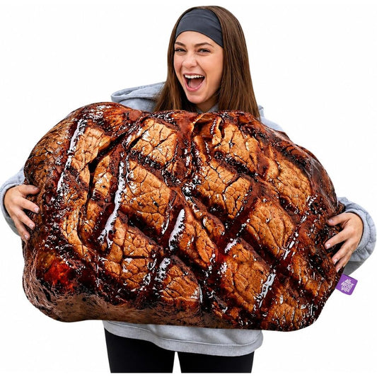 A woman holding a very large plush pillow designed to look like a grilled steak with glossy sauce, against a plain white background.