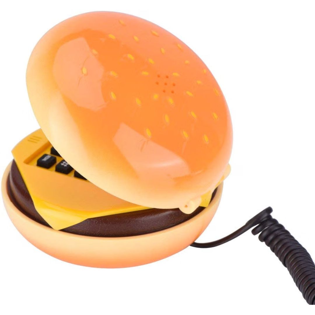 A novelty toy telephone shaped like a hamburger, with a glossy orange bun, yellow cheese layer, dark brown patty, and a black coiled cord, shown on a plain white background.