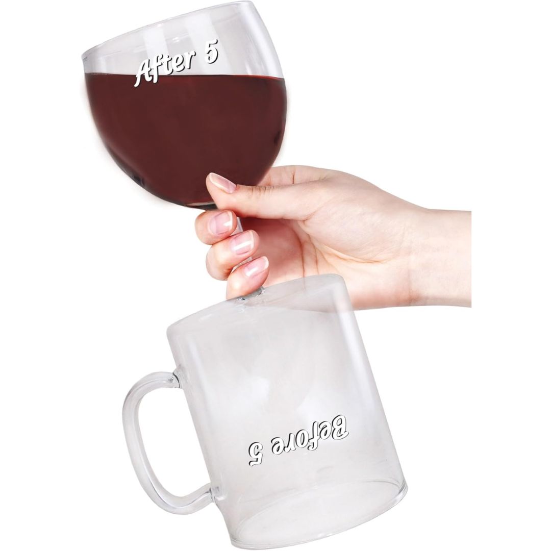 A hand holds a funny coffee and wine reversible glass filled with dark red wine with a matching clear glass mug with a handle on the other end. Both glasses have the words 'Before 5' and 'After 5' printed in white script, set against a plain white background.