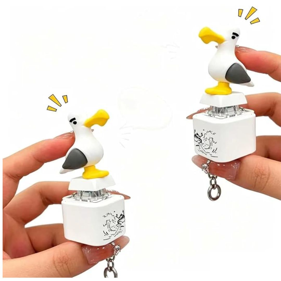 Two hands holding small seagull-shaped keychain fidget toys against a plain white background. The toys have white bodies, yellow beaks and feet, and gray wings, with cartoon seagull drawings printed on the small white rectangular bases.