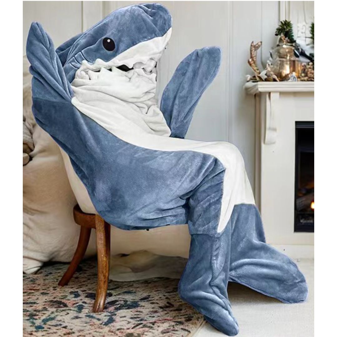 A person wearing a plush shark-shaped onesie sitting in a chair styled in a cozy living room setting.