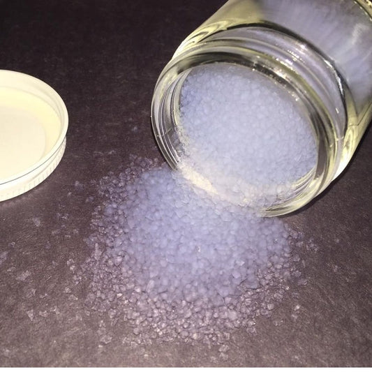 Silica aerogel frozen smoke spilled from a clear glass jar onto a dark gray surface, with the white lid resting to the left.