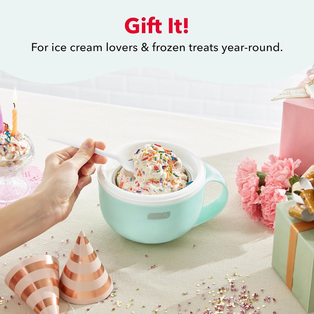 A hand holds a white spoon into a mint green electric ice cream maker bowl filled with vanilla ice cream and colorful sprinkles, set on a decorated tabletop with pink flowers, gift boxes, and party hats. Text at the top reads 'Gift It! For ice cream lovers & frozen treats year-round.