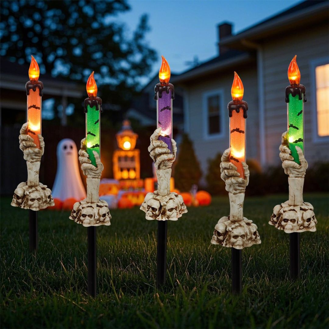 Halloween-themed decorative candles with skeleton hands on stakes in a yard.