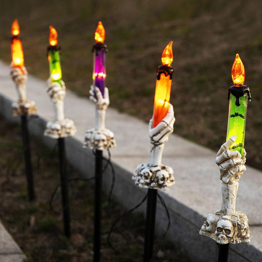 Decorative candles with skeleton hands holding colorful flames near a stone ledge.
