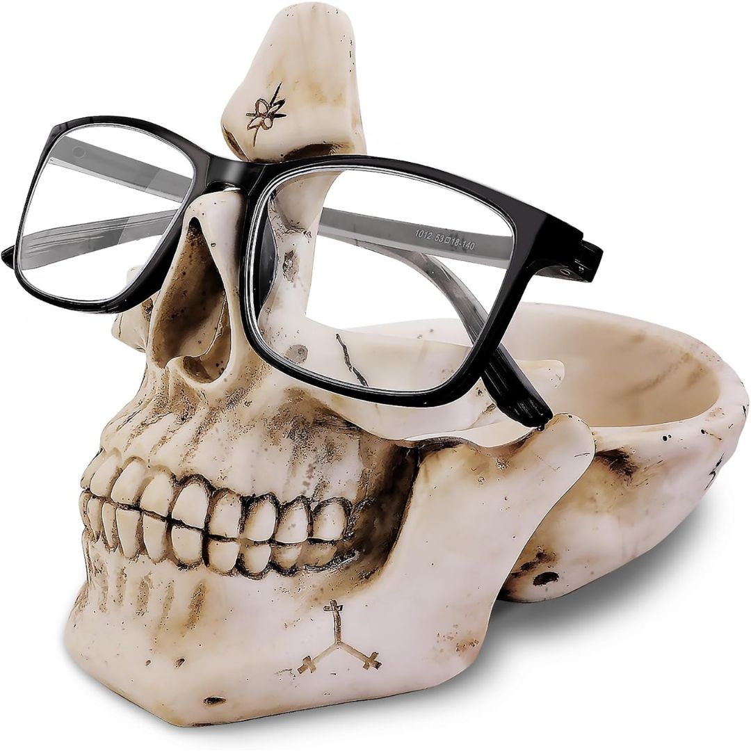 Black eyeglasses resting on a decorative skull-shaped holder photographed on a white background