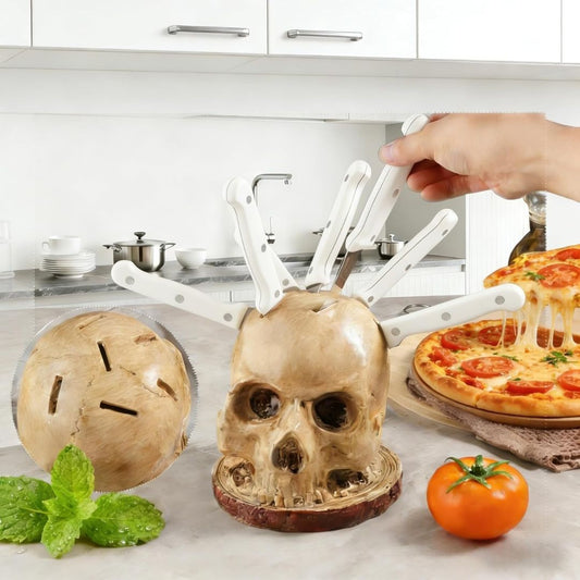 Skull-shaped knife holder on a kitchen counter with a pizza and tomato in the background.
