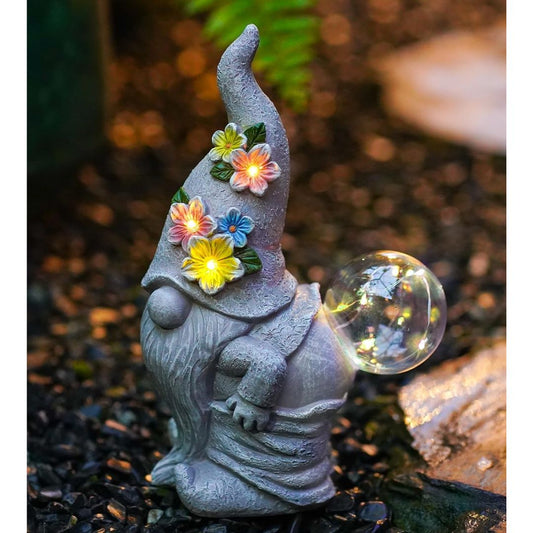A solar garden gnome with a glowing crystal ball in a garden setting.