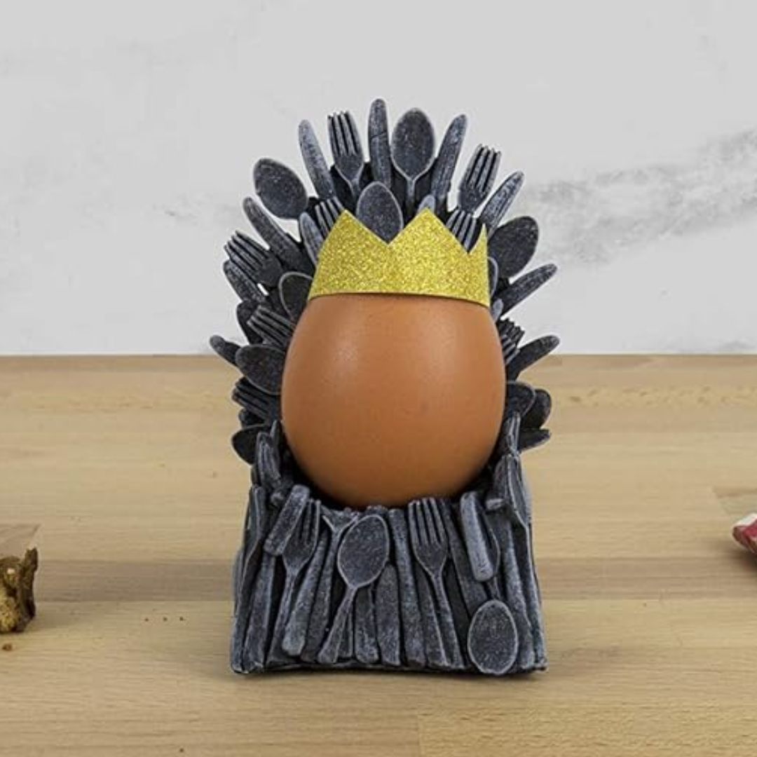 Egg in a holder shaped like The Iron Throne with a crown, on a wooden surface.