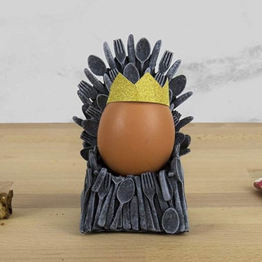 Egg in a holder shaped like The Iron Throne with a crown, on a wooden surface.