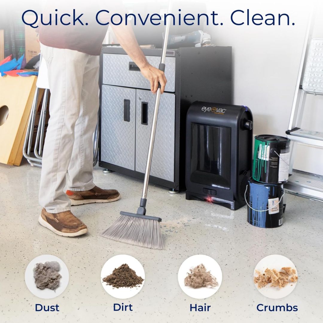 Person using a broom to clean a garage floor with cleaning products displayed with a touchless vacuum dustpan nearby.