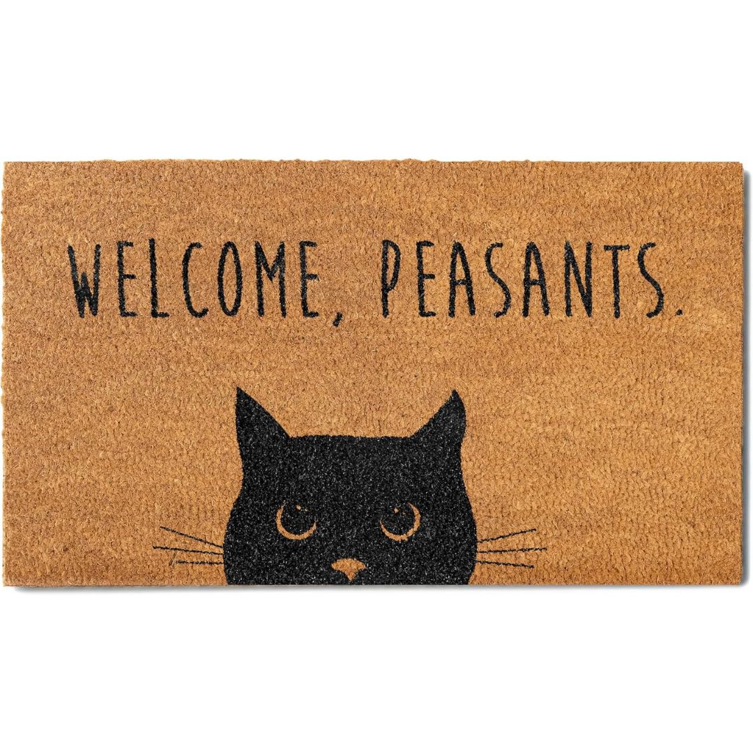 A rectangular natural coir doormat with the text 'WELCOME, PEASANTS.' in black and a black cat face graphic at the bottom, shown on a plain white background.