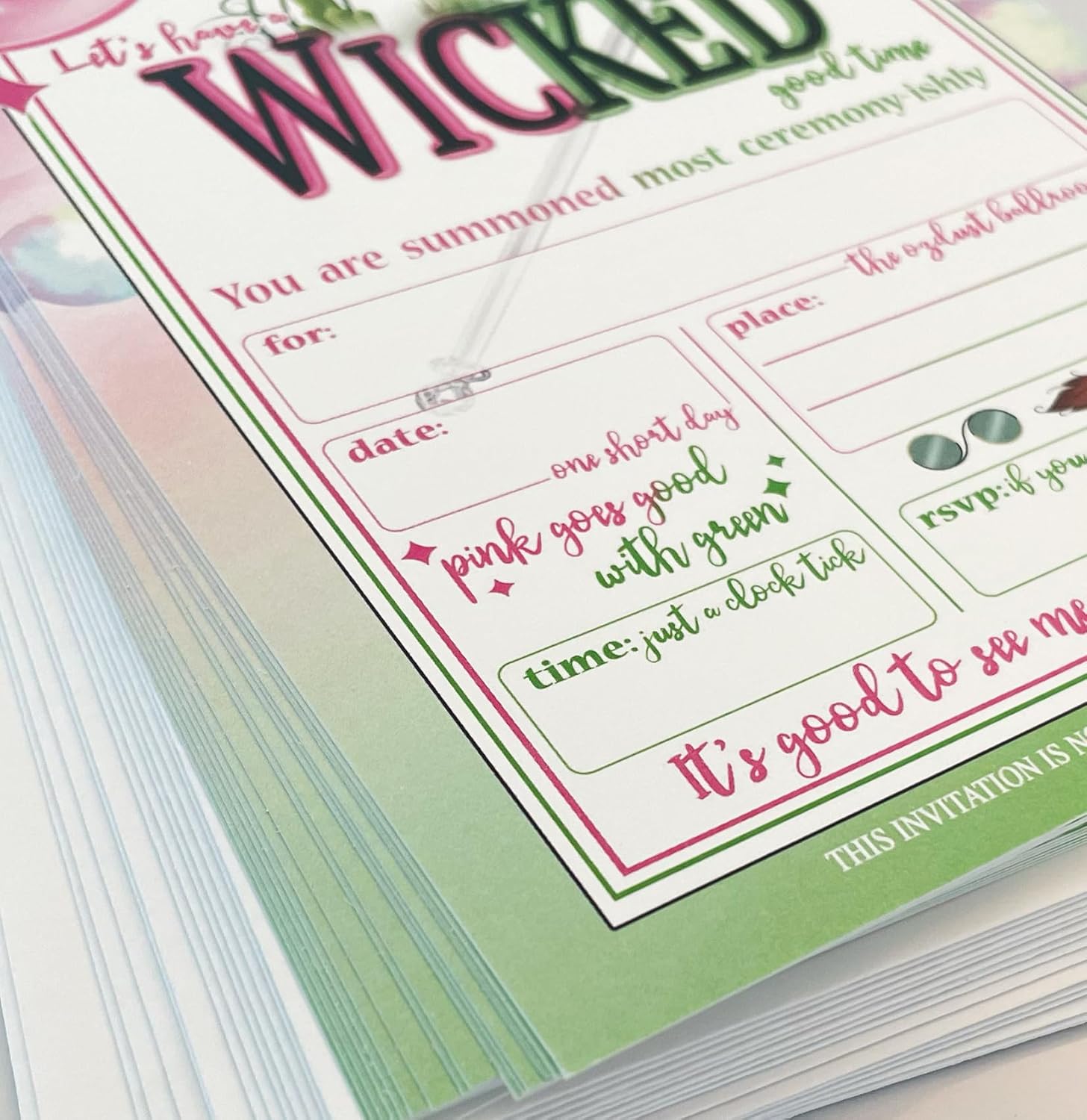 A stack of "Wicked" themed invitations in pink and green, with balloons and a witch hat. Text: "LET'S HAVE A WICKED GOOD TIME" and "YOU ARE SUMMONED MOST CEREMONY-ISHLY."