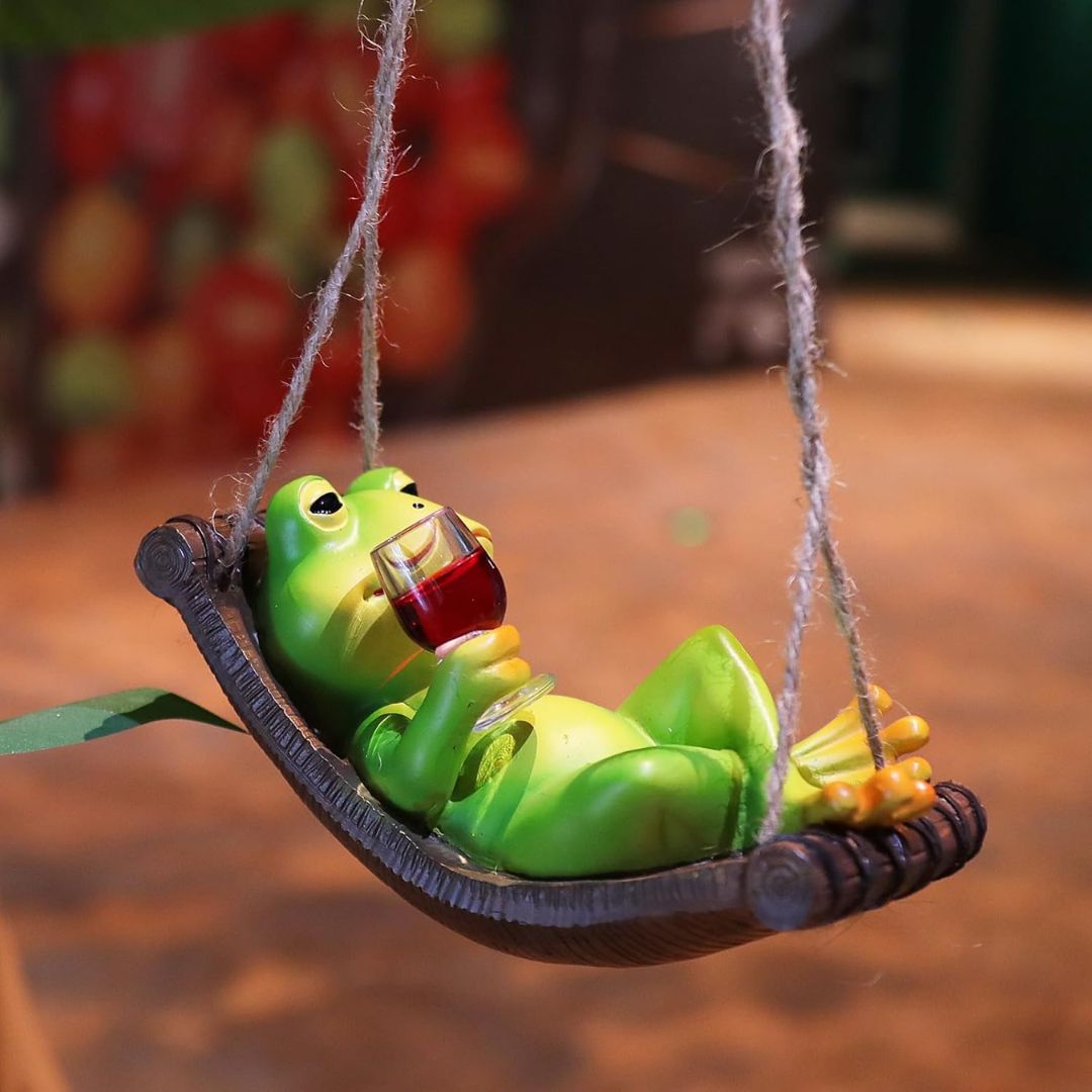 Frog figurine on a swing with a glass of wine, blurred background