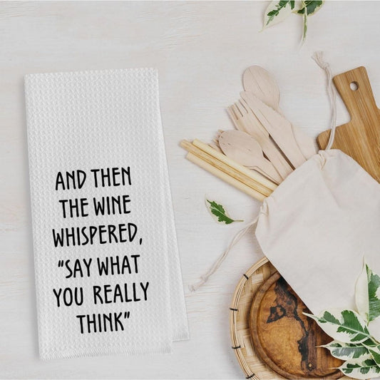 White towel with humorous text next to wooden cutlery and a bag on a light surface.