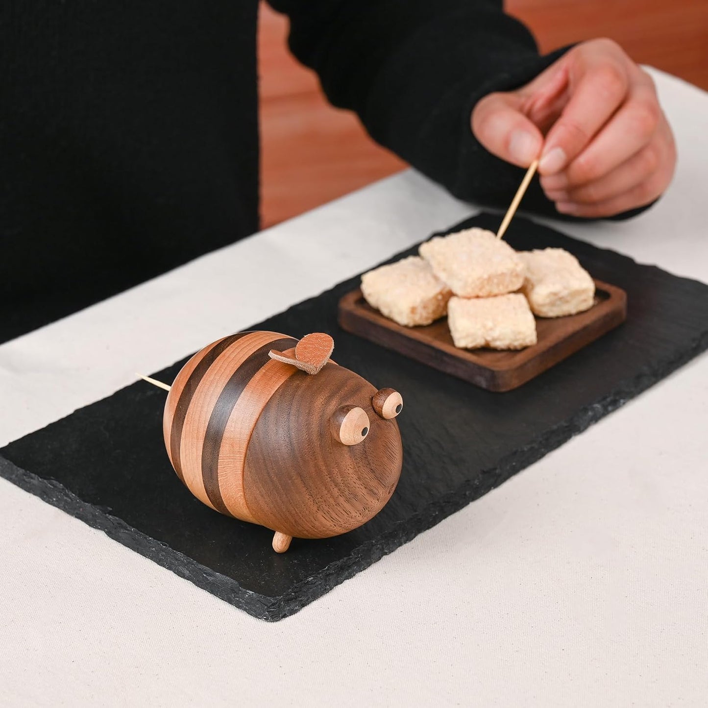 Wooden bee-shaped toothpick holder with food on a slate board.