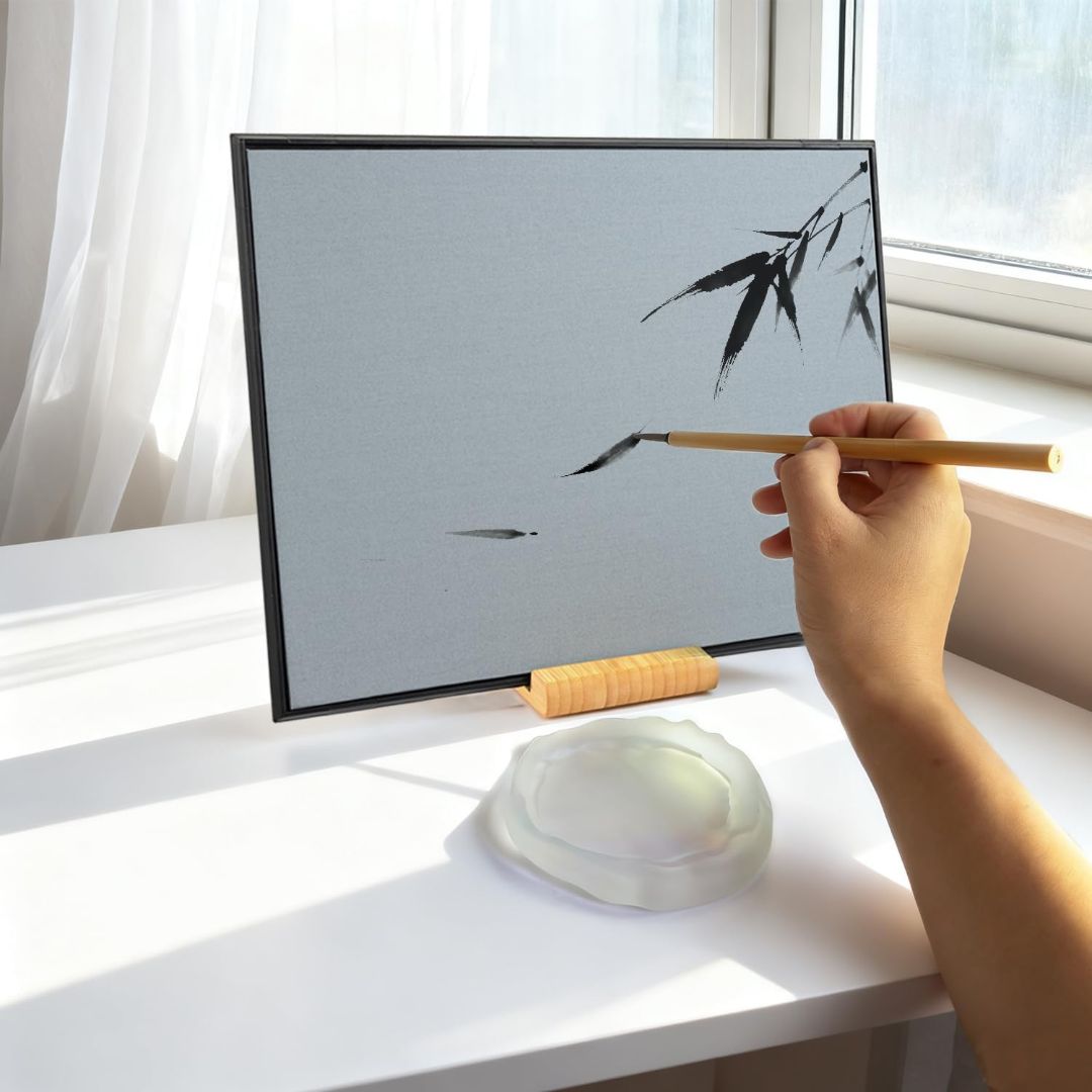 Hand painting bamboo with water on a reusable Zen drawing board beside a small water dish