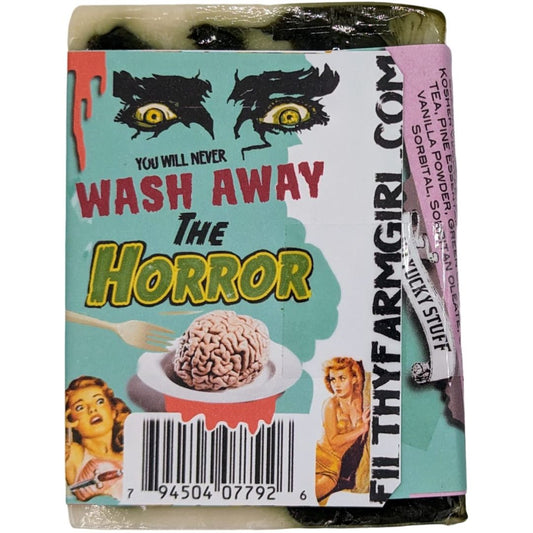 A packaged bar of soap labeled 'Wash Away The Horror' with retro horror artwork, including eyes, a brain on a plate, and illustrated women. The package is wrapped in clear plastic and sits on a plain white background.