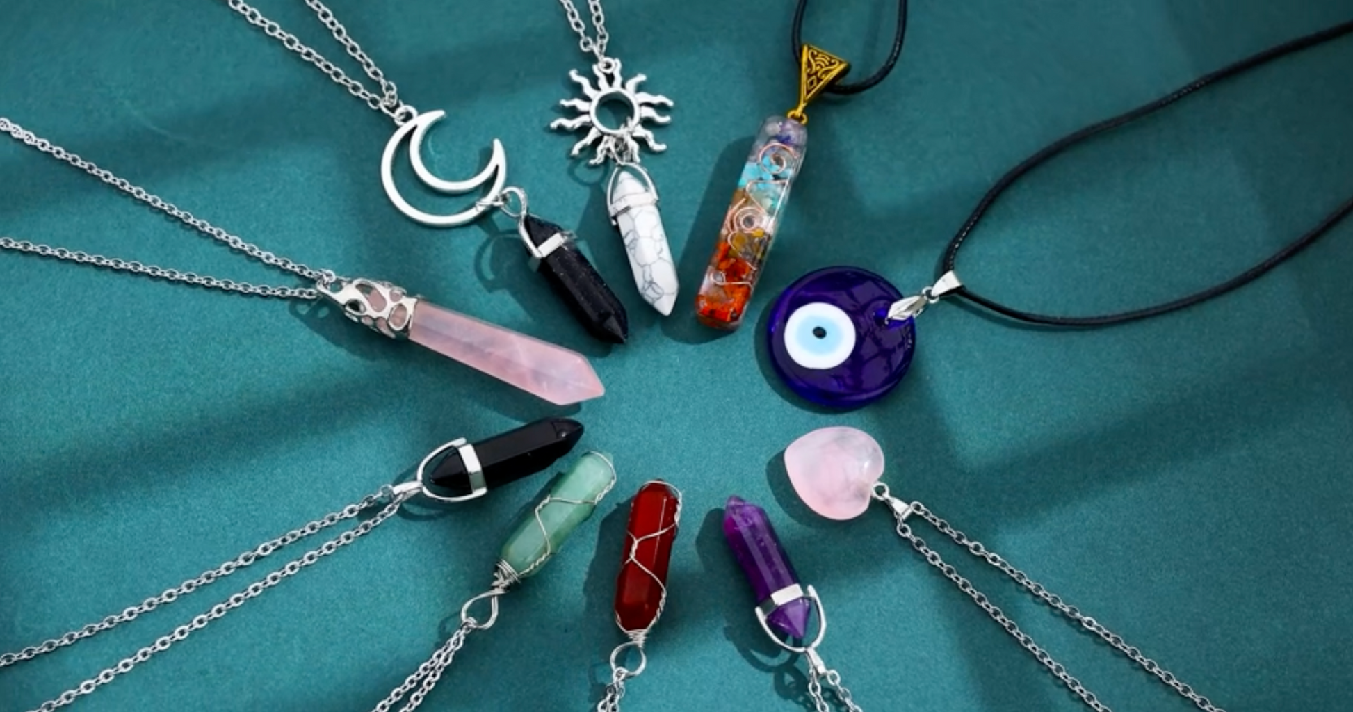 10 crystal necklaces arranged in a circle on a green felt cloth. Each necklace has a silver chain or black rope and they all feature a different colored crystal pendant.