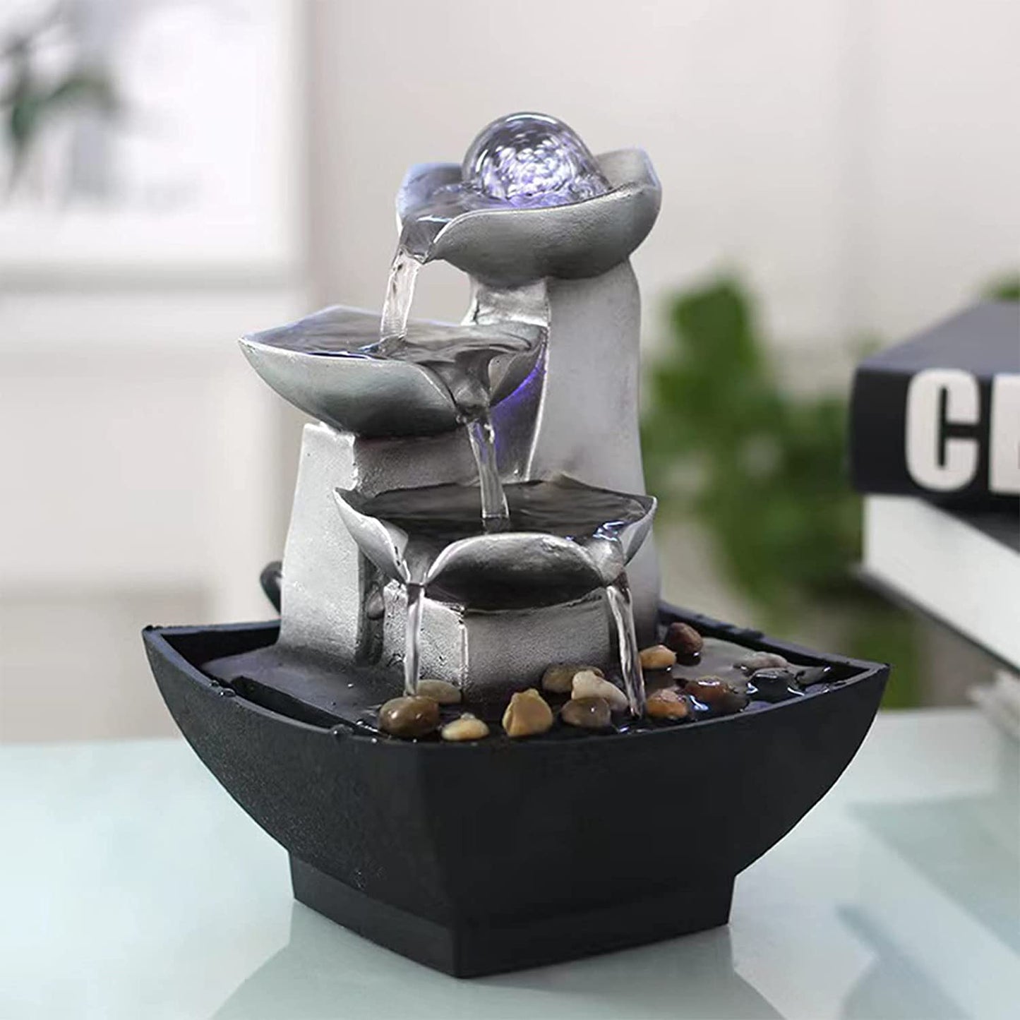 A calming tabletop 3-tier fountain with water cascading down 3 levels into the base which is filled with water and rocks.