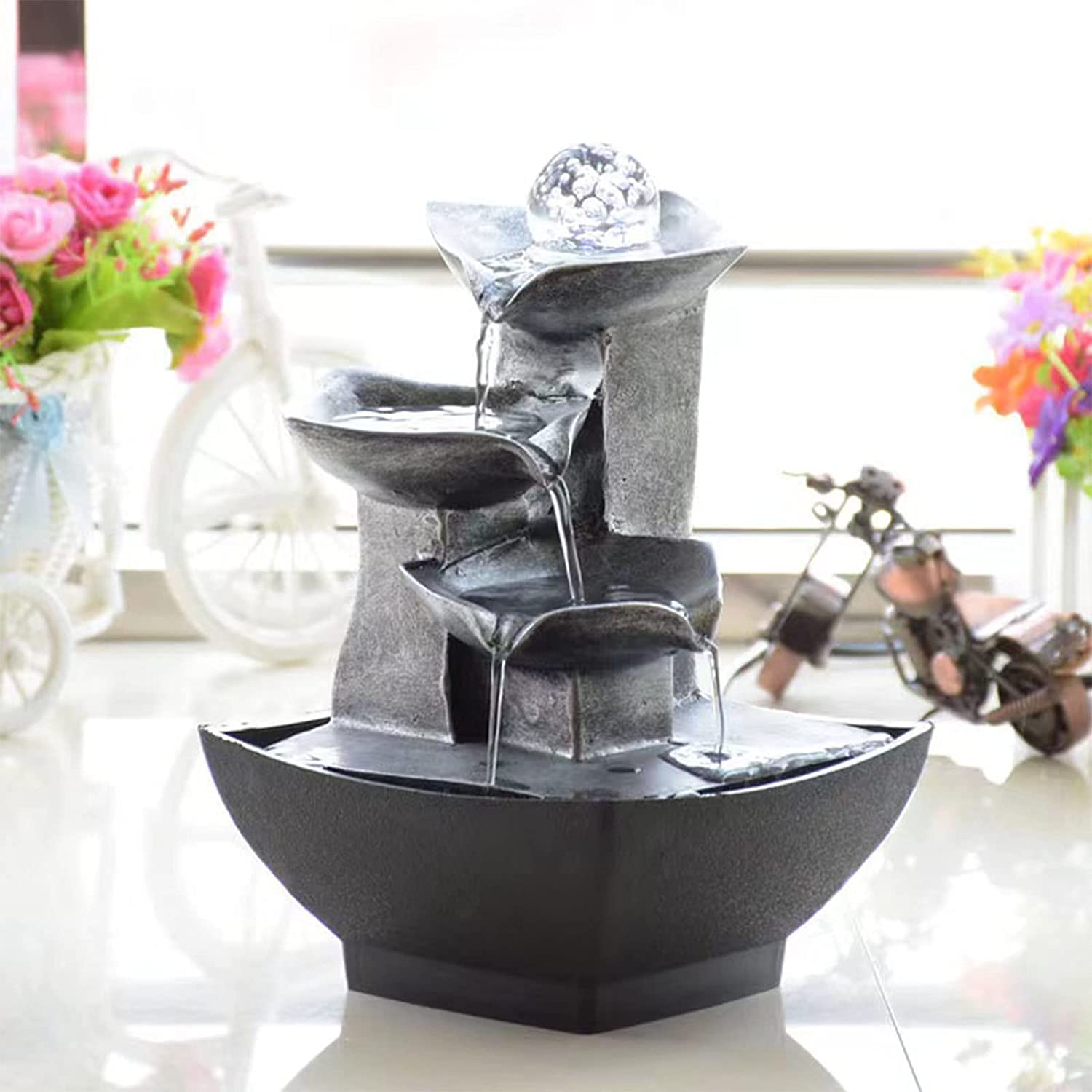 A tabletop fountain with 3 levels sits on a desk. Water is flowing down the 3 levels.